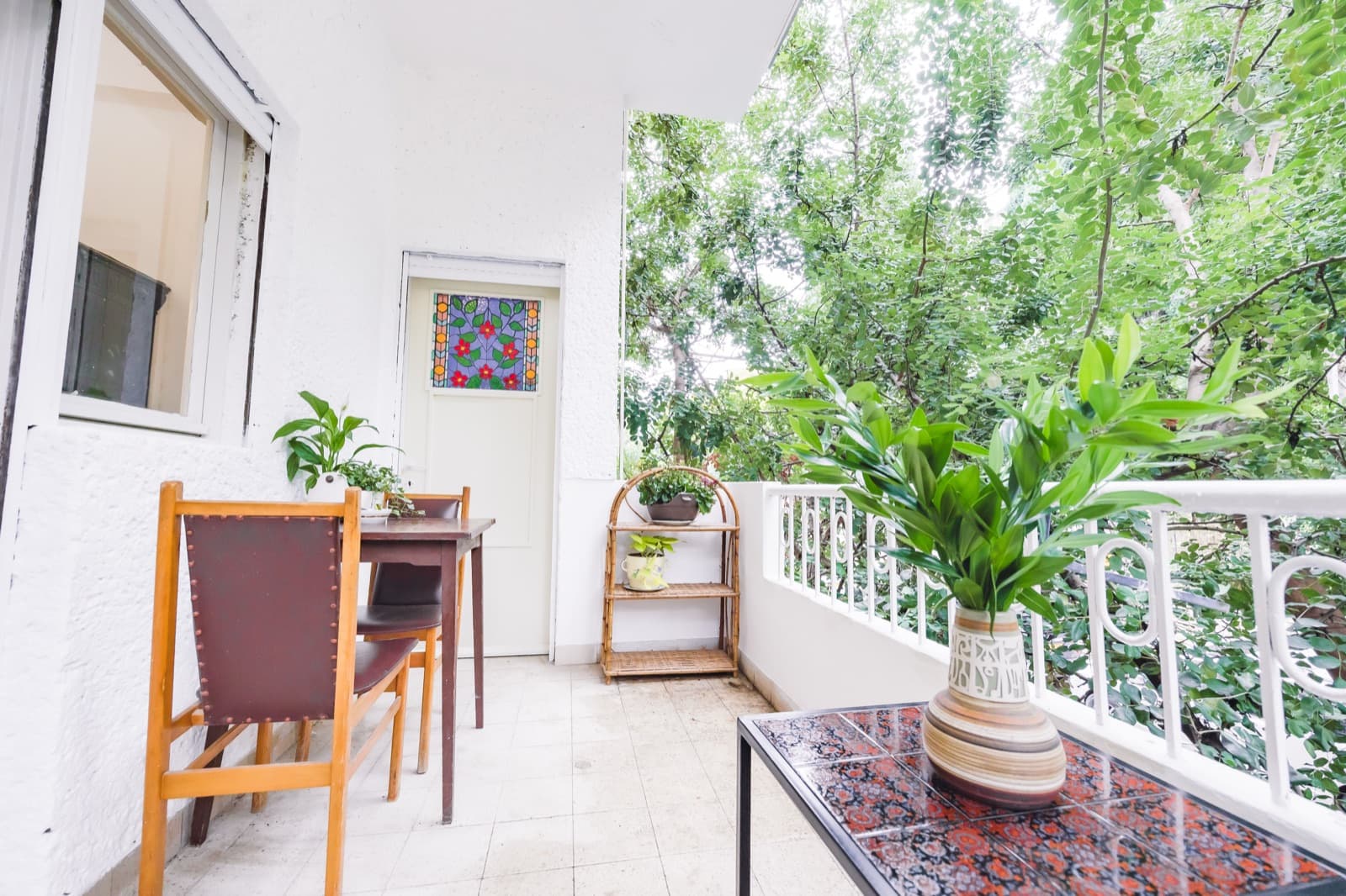 Second balcony with table and chairs surrounded by green treetops in Haifa